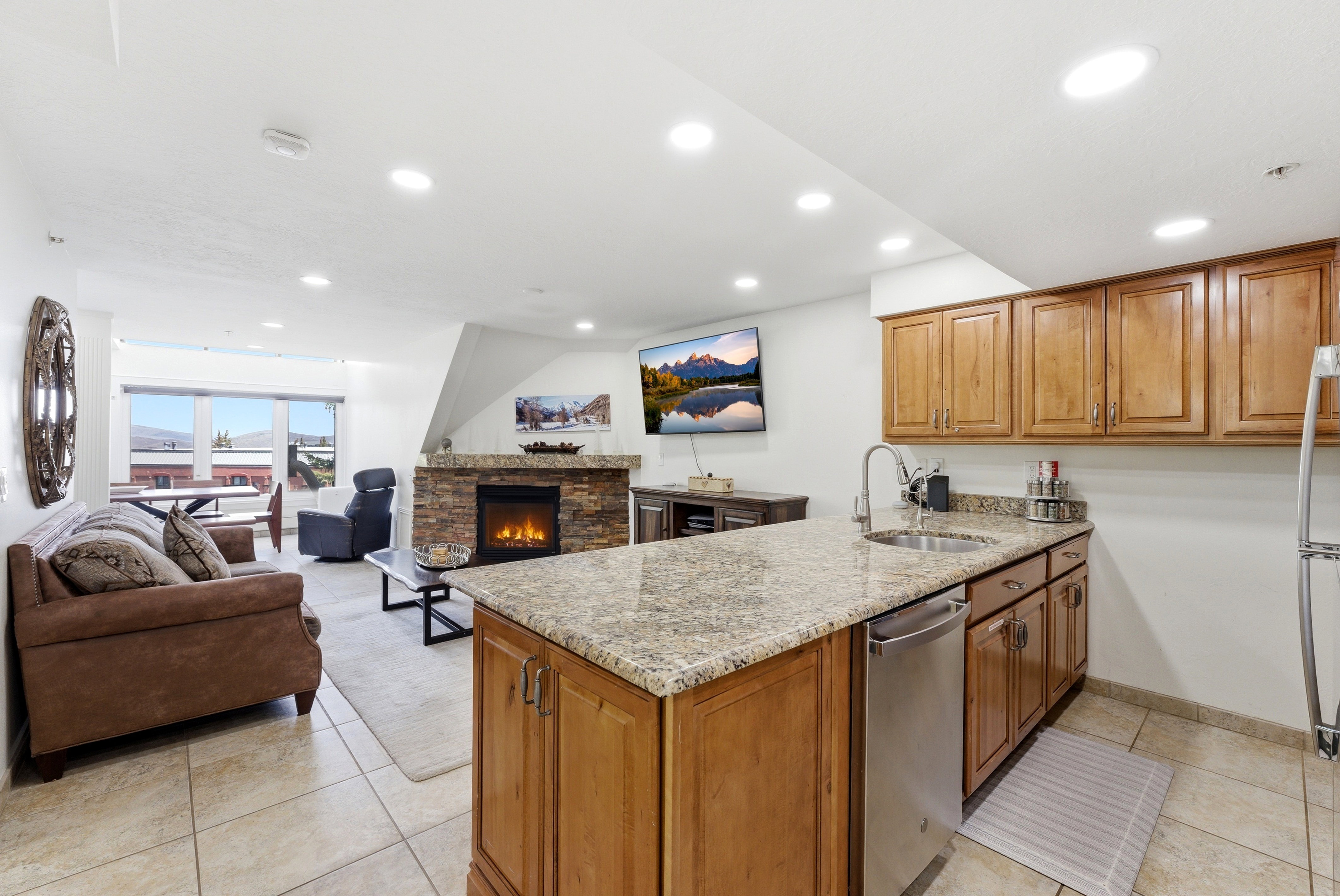 Kitchen with a peninsula, light stone counters, a stone fireplace, wood finish cabinets, and recessed lighting