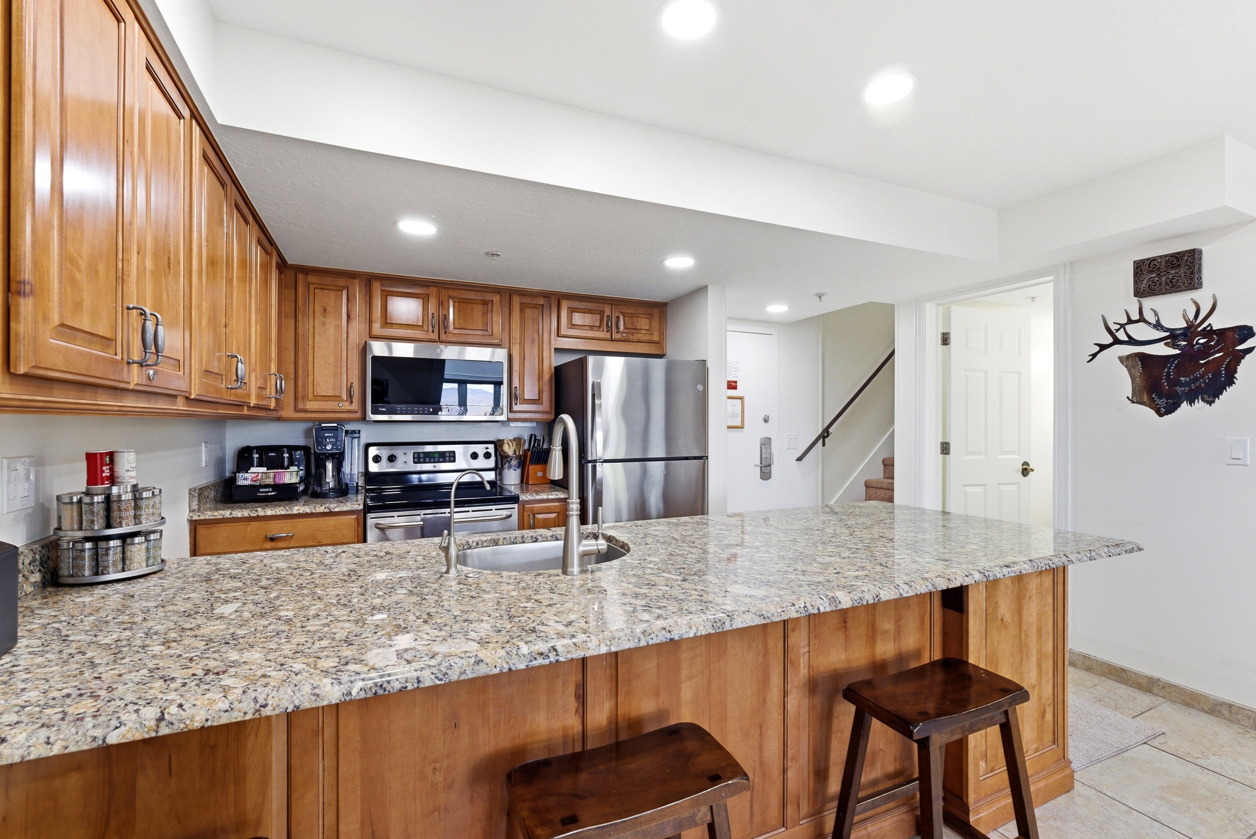Kitchen featuring a peninsula, wood finish cabinetry, light stone counters, stainless steel appliances, and a kitchen breakfast bar