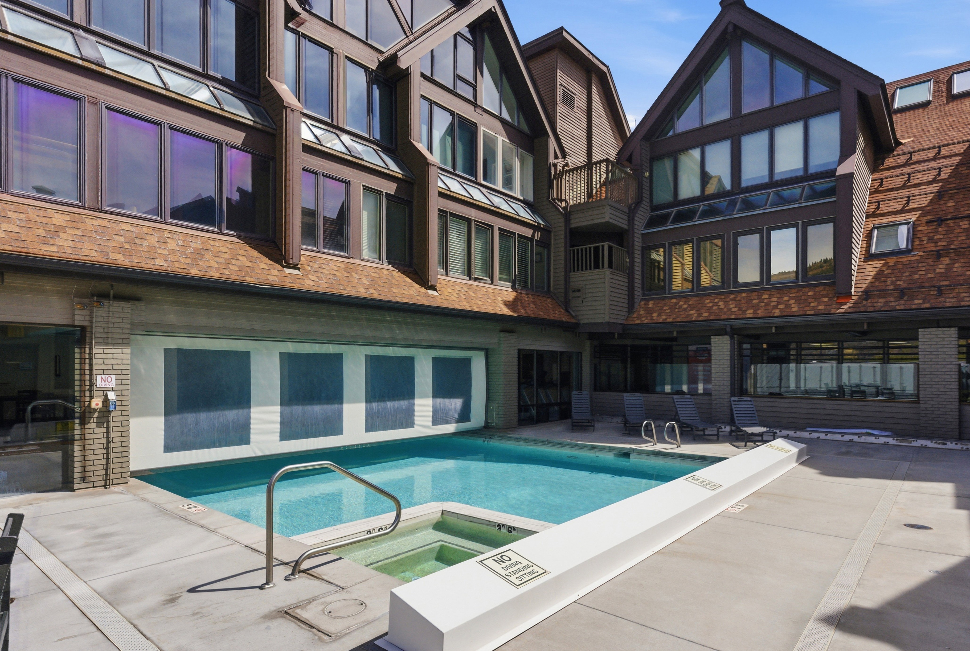 Back of property featuring brick siding, a pool with connected hot tub, a balcony, and a patio area