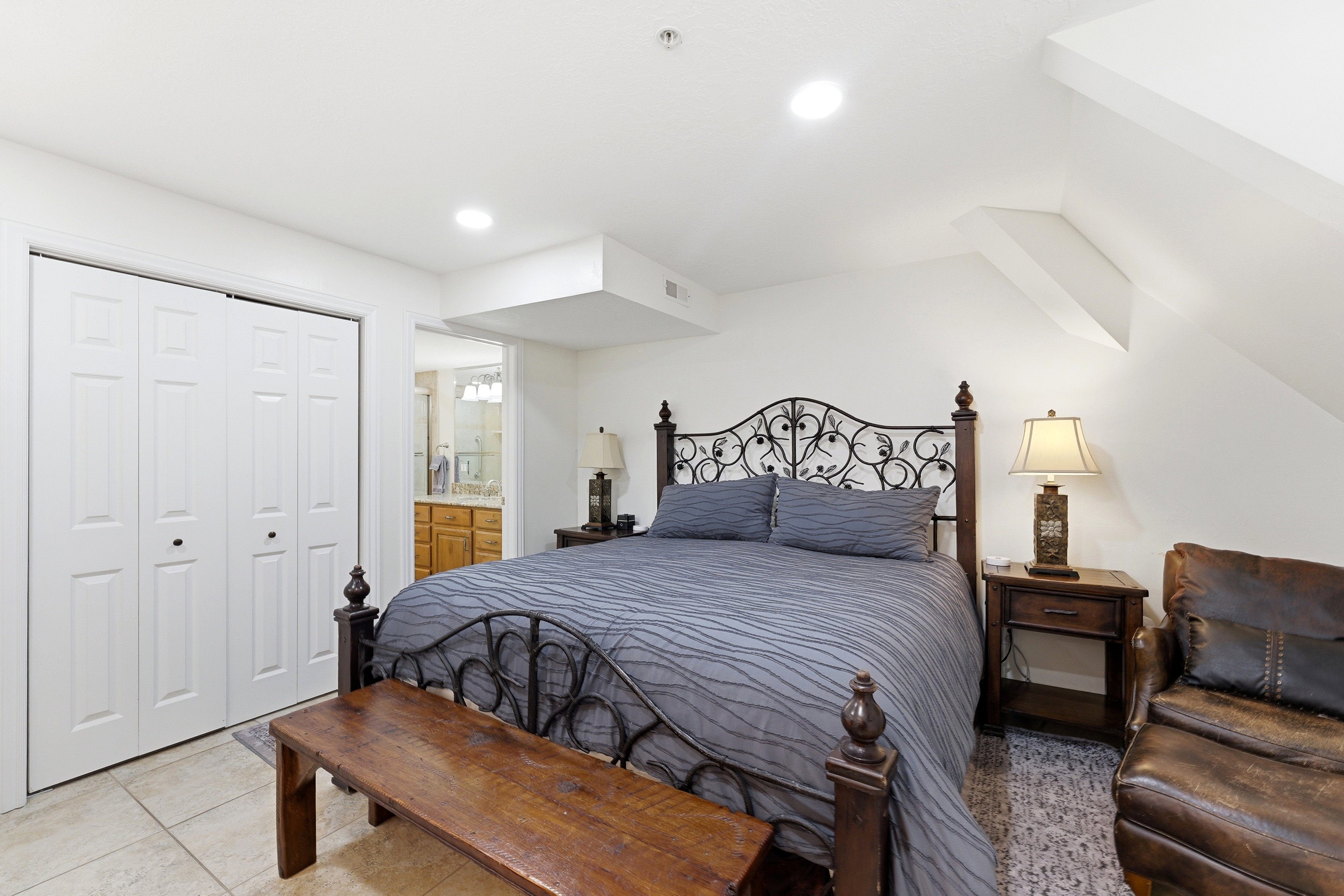Bedroom with light tile patterned flooring, ensuite bathroom, a closet, and lofted ceiling