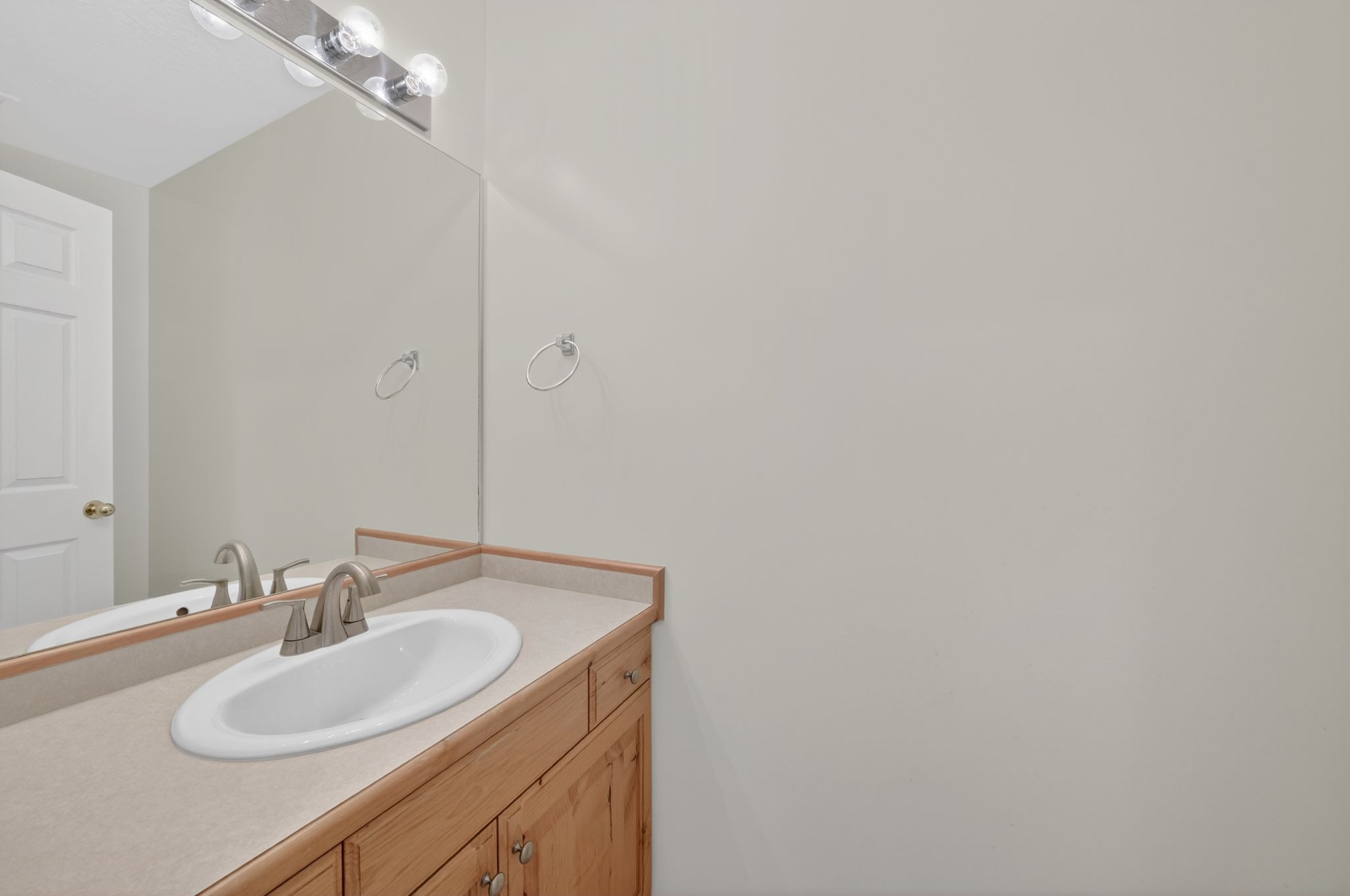 Half Bathroom vanity featuring a light-toned countertop with an integrated oval sink, a brushed nickel faucet, and natural wood cabinetry