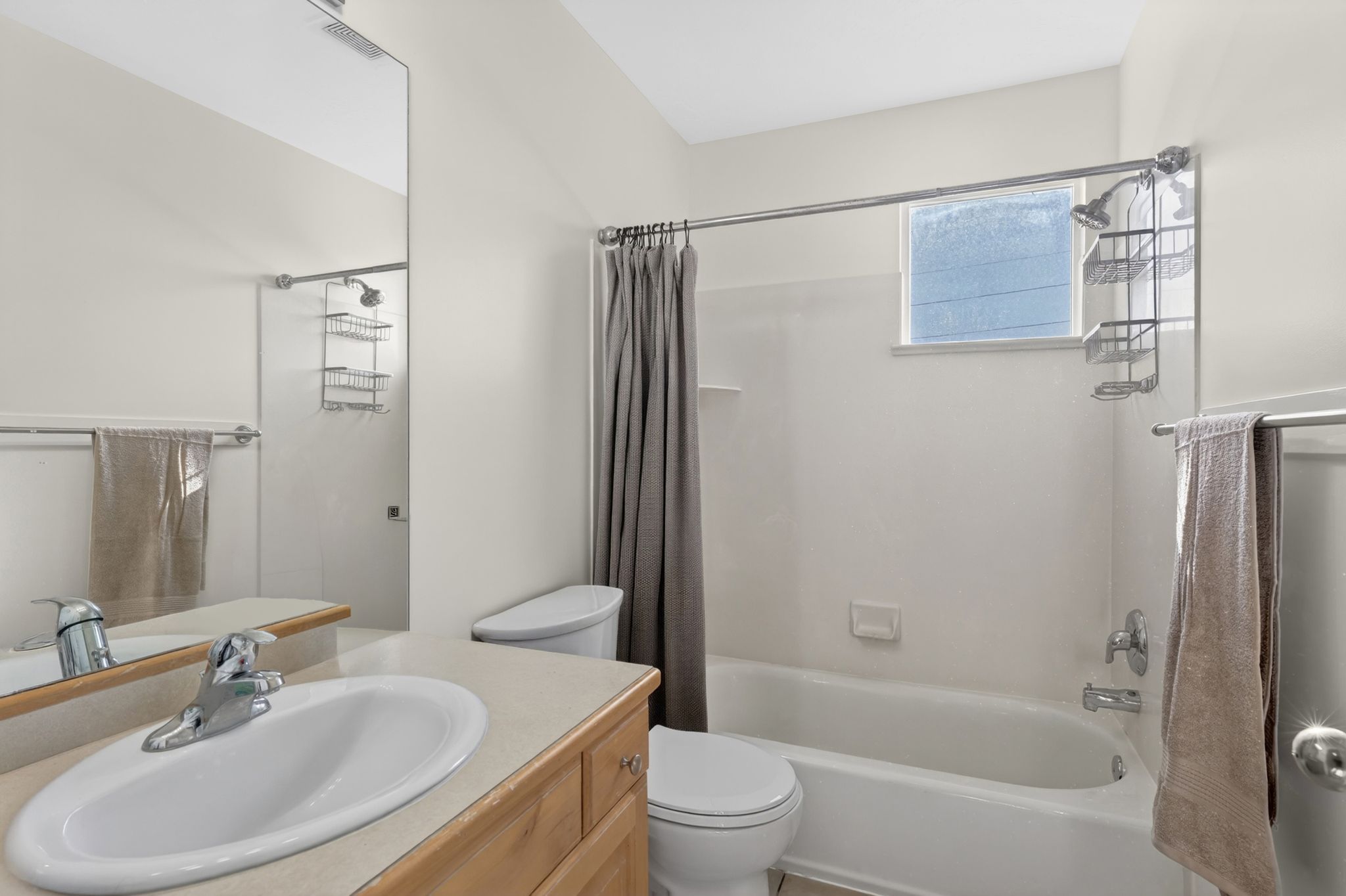 Bathroom featuring a vanity with a light-toned countertop and integrated sink, a full-width wall mirror, a toilet, and a combination shower/tub with a window