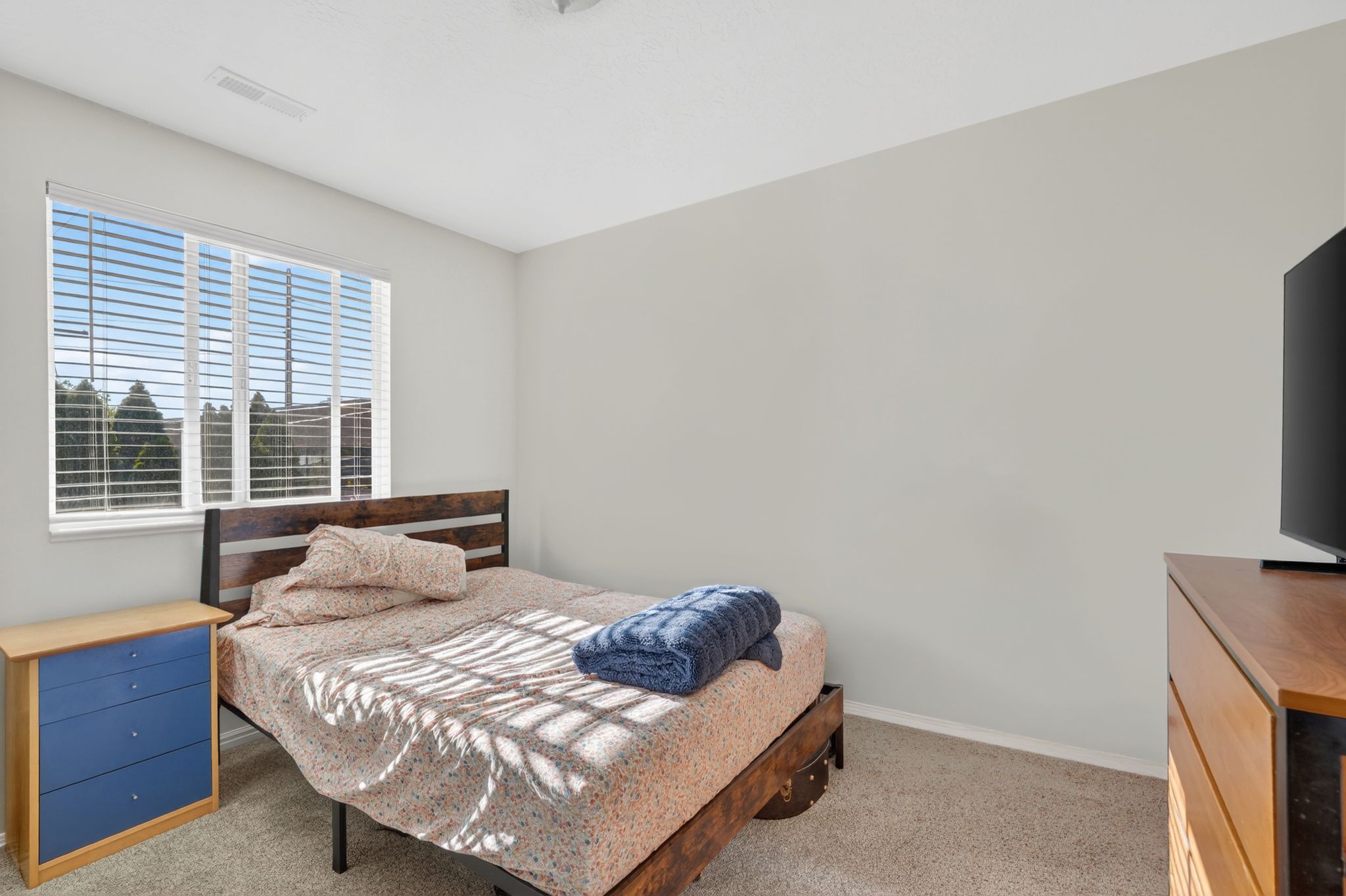 Bedroom featuring a large window with white blinds, neutral wall paint, and carpet flooring