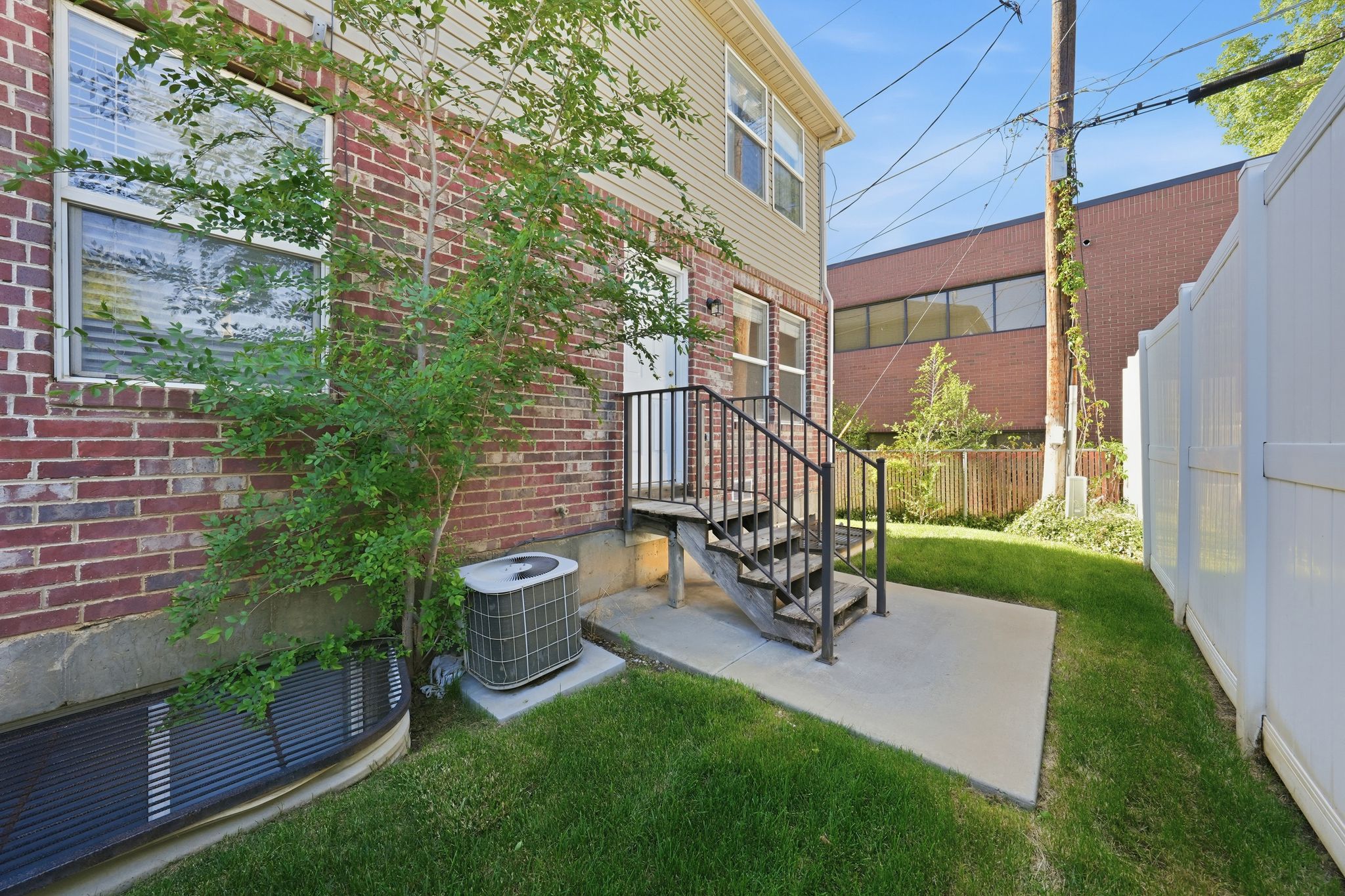 Rear exterior featuring a concrete patio, wood stairs with metal railings, a brick facade, and a white privacy fence
