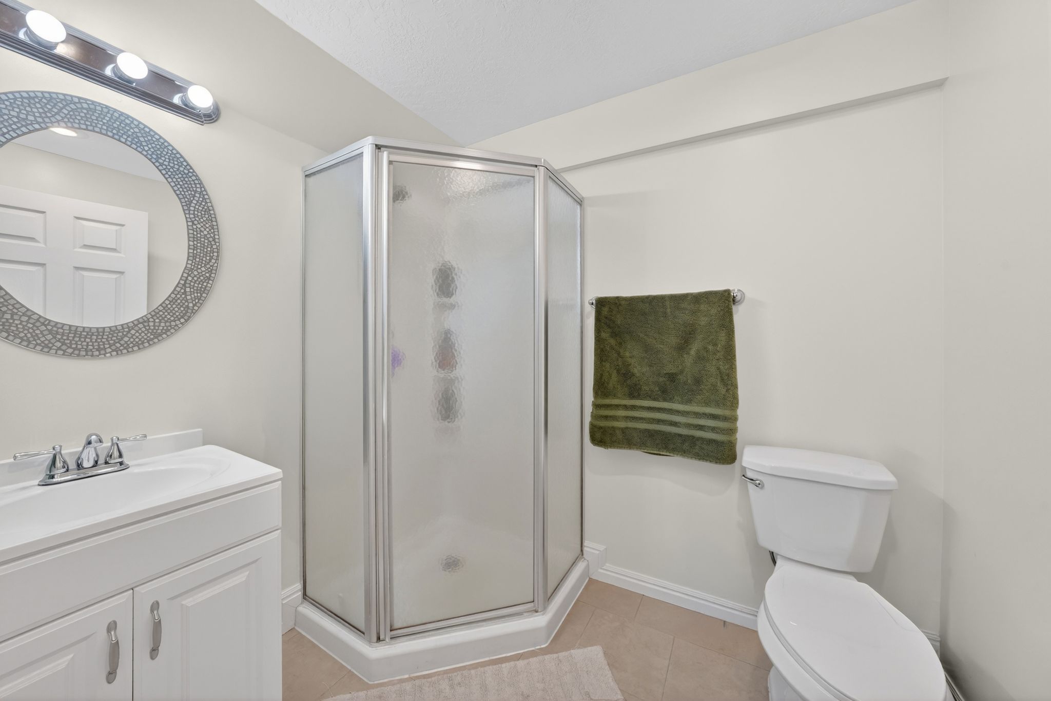 Compact bathroom featuring a corner shower with frosted glass enclosure, a vanity with an integrated sink, a circular mirror with a decorative frame, and a white toilet
