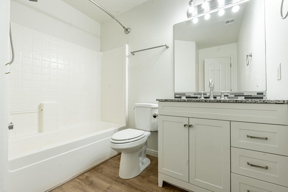 Bathroom featuring wood-finish flooring, a white vanity with shaker-style cabinetry, and a stone-finish countertop