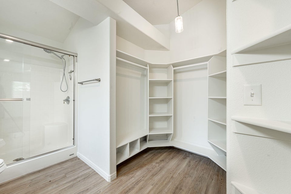 Walk-in closet featuring extensive built-in shelving and hanging rods, wood-finish flooring, a contemporary pendant light fixture, and an adjoining glass-enclosed shower with polished chrome fixtures