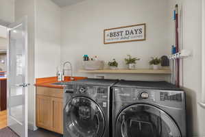 Dedicated laundry area featuring a utility sink with a high-arc faucet, wood-finish cabinetry, and a floating shelf