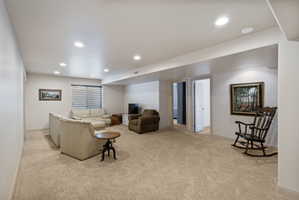 Spacious carpeted living area with recessed lighting, offering neutral wall tones and a visible window with horizontal blinds