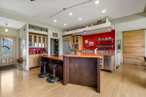 Expansive kitchen featuring a double island with integrated cooktop, stainless steel appliances, vibrant red accent wall, and light wood-finish flooring