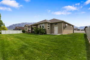 Expansive rear yard featuring a manicured lawn, a full-height privacy fence, and mountain scenery