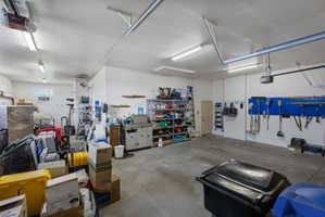 Spacious garage featuring a concrete floor, bright overhead fluorescent lighting, white painted walls, a side door, and an automatic garage door opener
