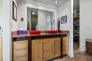 Dual vessel sinks with modern fixtures, stone countertop, built-in mirror, wood-finish vanity with drawer and cabinet storage, and tiled flooring