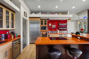 Contemporary kitchen featuring an integrated cooktop on the island, stainless steel appliances, vibrant orange countertops, light wood-finish cabinetry, and recessed ceiling lighting