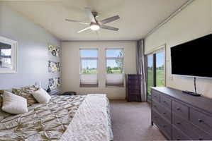 Carpeted bedroom featuring a contemporary ceiling fan, two large windows with horizontal blinds, and a sliding glass door providing exterior access