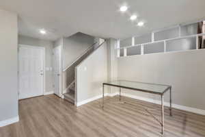 Open-concept space featuring wood-finish flooring, recessed lighting, a white paneled entry door, a carpeted staircase with a white handrail, and built-in shelving