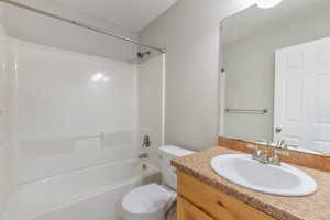 Bathroom featuring a vanity with a light-toned countertop, an undermount sink with dual-handle faucet, a large frameless mirror, and a white shower/tub combination with a chrome shower rod