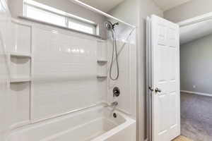 Bathtub and shower combination featuring a white tiled surround with integrated shelving