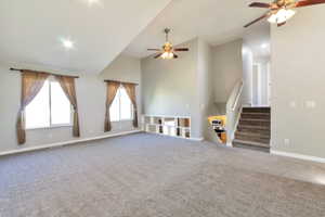 Spacious living area featuring vaulted ceilings, plush carpet flooring, and two ceiling fans