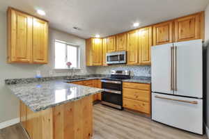 Kitchen featuring light wood cabinetry, light-toned countertops, stainless steel appliances including a microwave and range, and a white refrigerator with gold-tone hardware