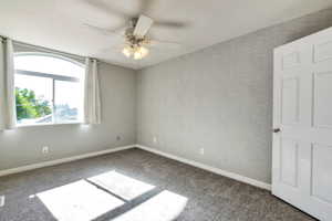 Bedroom featuring a large arched window, textured accent wall, ceiling fan with integrated lighting, and neutral carpet flooring