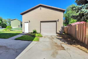Two-story detached garage featuring tan siding, a single garage door, a side entry door, and two exterior light fixtures