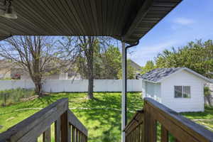 Expansive backyard featuring a detached storage shed with a shingled roof, a white privacy fence, and mature trees