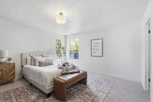 Bright bedroom featuring multiple windows, neutral wall paint, textured carpeting, a flush mount ceiling light fixture, and white trim