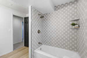 Bathtub shower featuring patterned tile surround, brushed nickel fixtures, and an integrated corner shelf