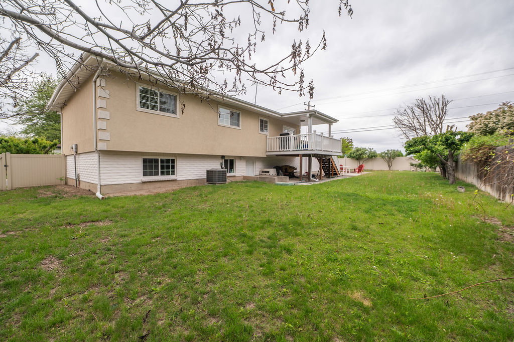 Expansive rear yard featuring a covered upper deck with white railings, a lower concrete patio, and a fully fenced perimeter