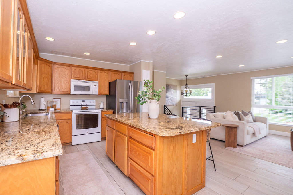 Kitchen featuring light wood cabinetry, granite countertops, white oven with matching microwave, and stainless steel refrigerator