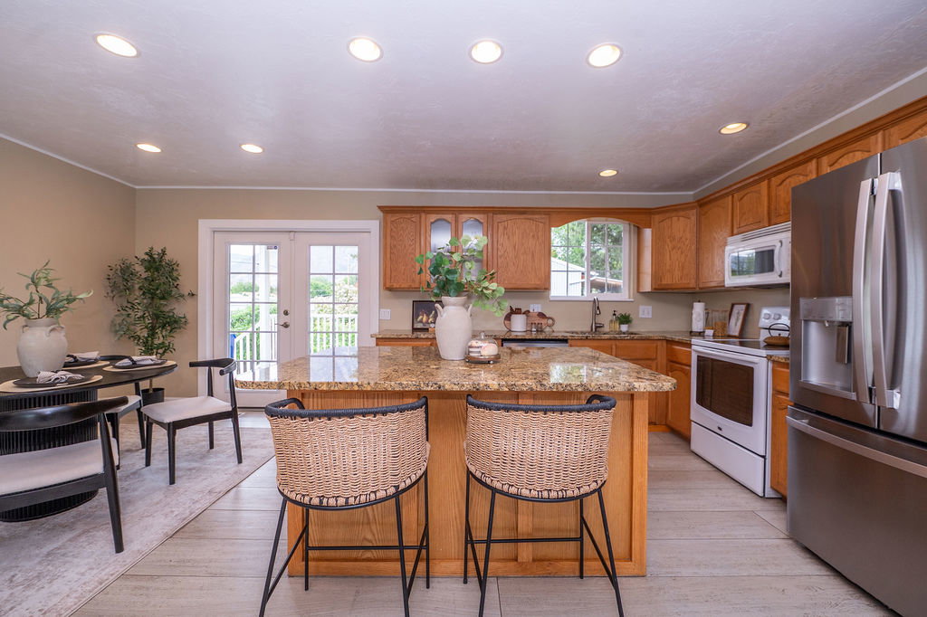Kitchen featuring light wood cabinetry, a granite-finish island with seating, stainless steel refrigerator, and white built-in appliances
