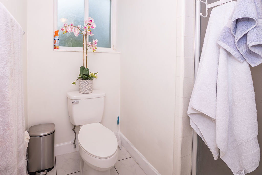 White toilet with a dual-flush mechanism, white baseboards, a frosted window, and light-toned tile flooring