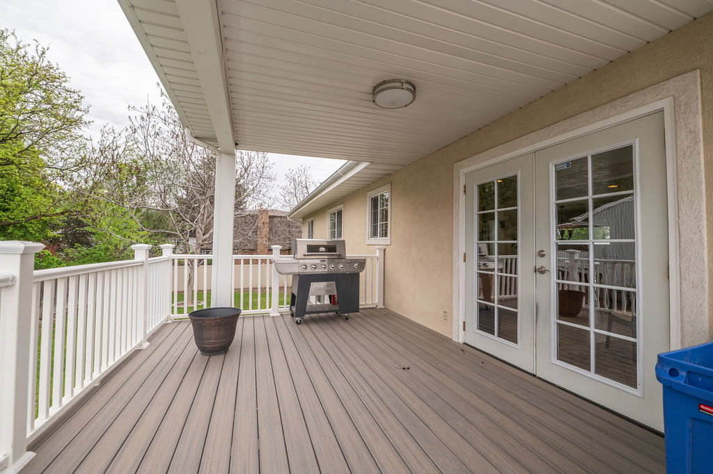 Expansive covered deck featuring composite decking, white railing, and double French doors with grid-patterned glass