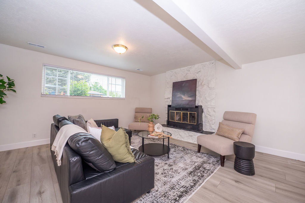 Living area featuring a stone-clad fireplace with a black insert, light wood-finish flooring, and white baseboards