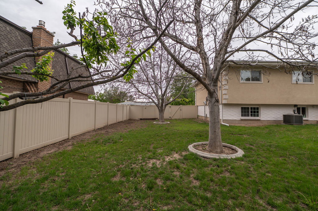 Fenced backyard with mature trees and a stucco-exterior home
