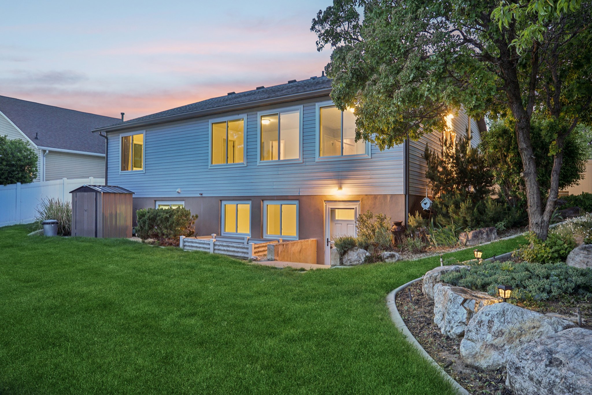Expansive grassy yard with tiered landscaping featuring rock retaining walls and mature trees
