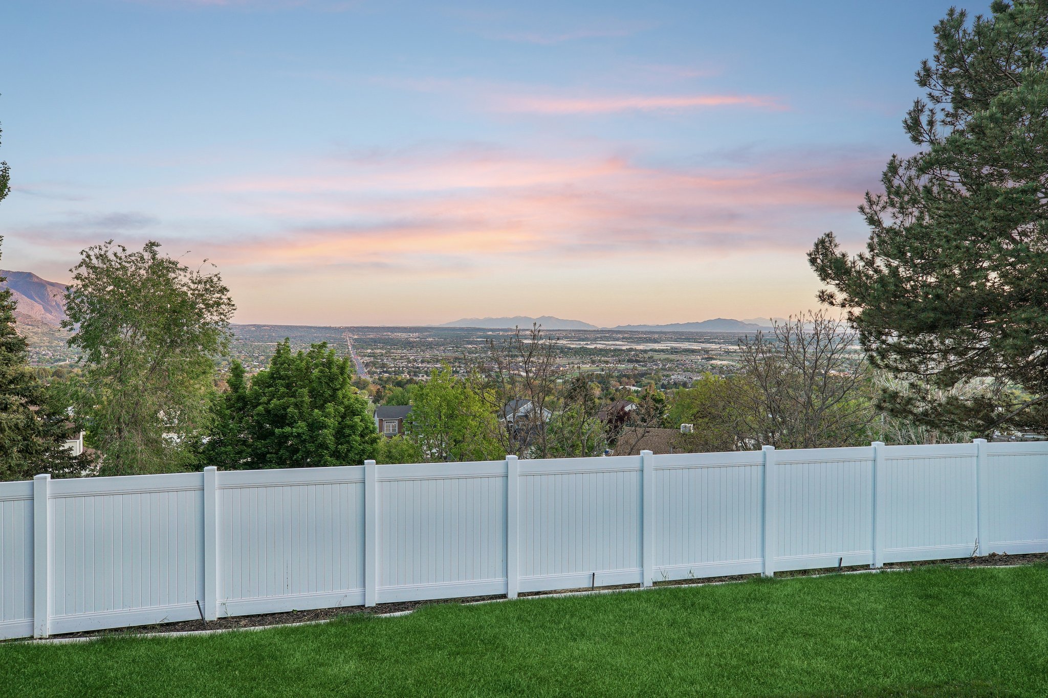 Expansive backyard featuring a manicured lawn, a full-height white privacy fence, and mature trees