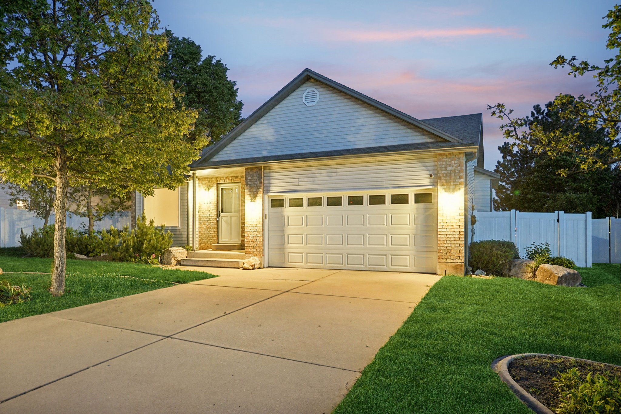 Single-family residence featuring a two-car garage with panel detailing, light brick accents, and a white privacy fence