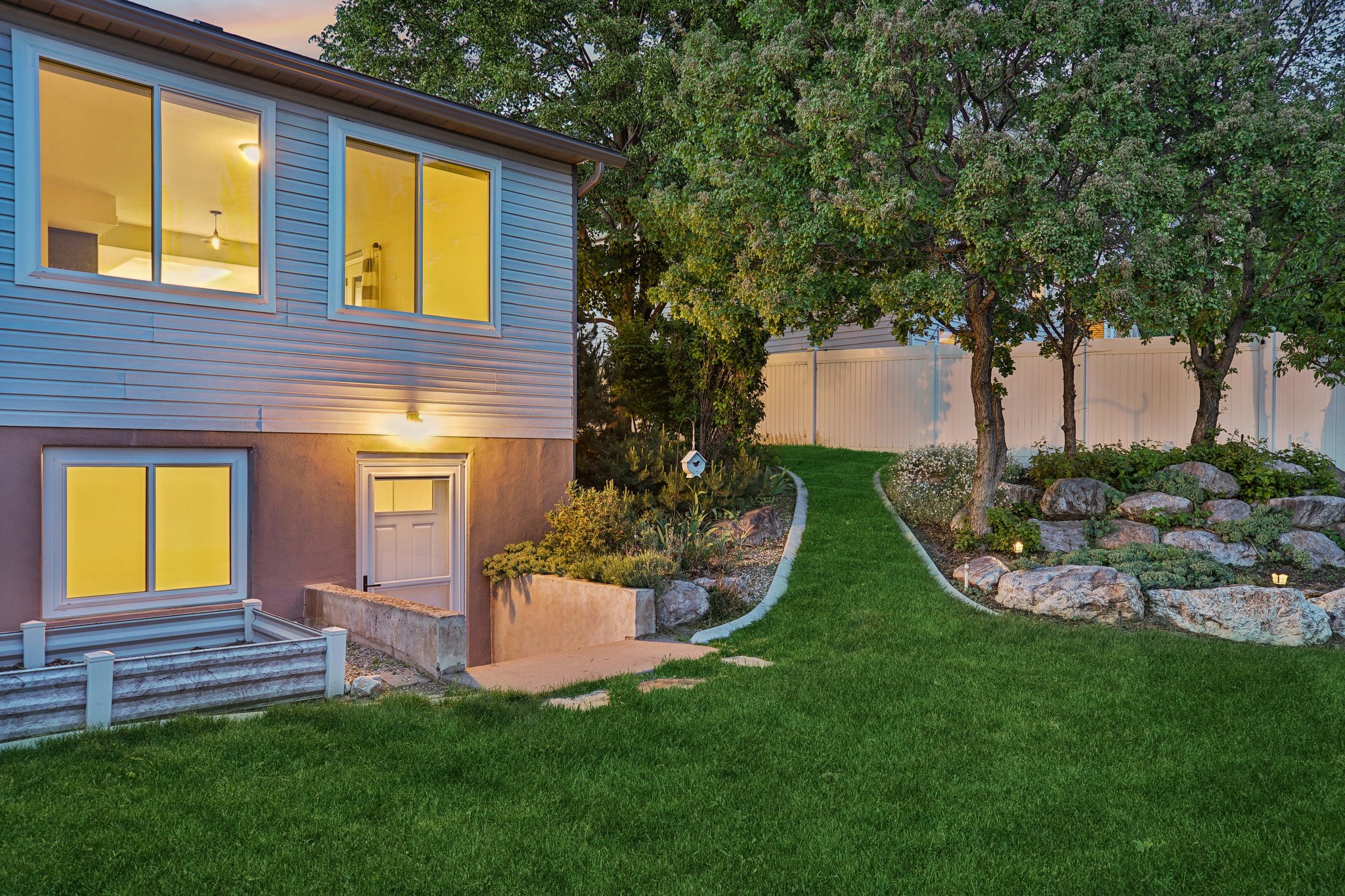 Expansive backyard featuring a manicured lawn, established trees, and decorative rock landscaping