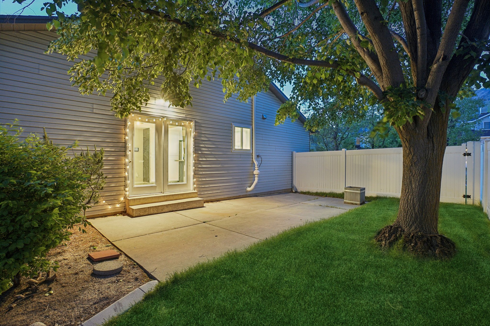 Private backyard featuring a concrete patio, established tree, and a white privacy fence