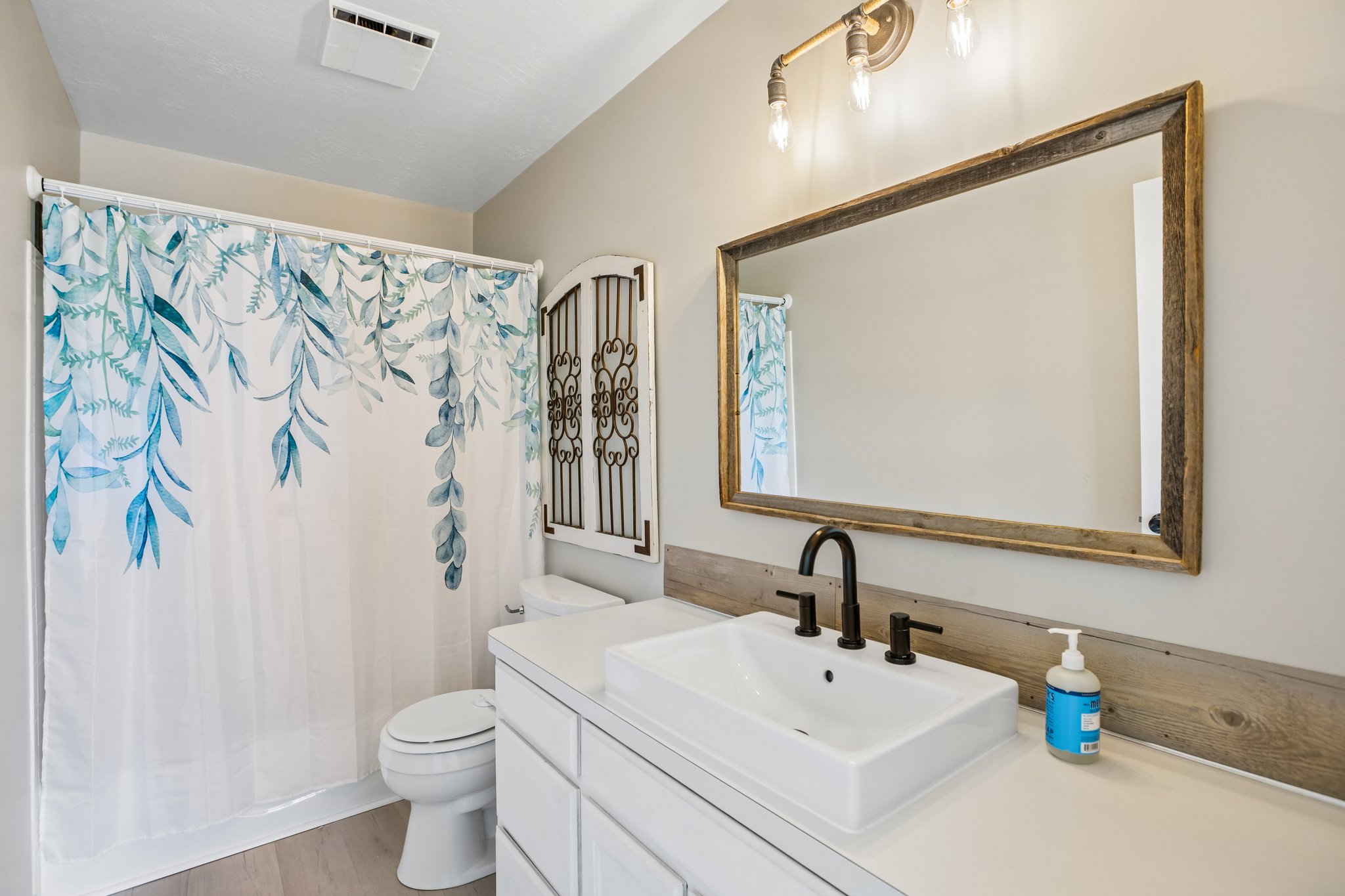 Bathroom featuring a floating vessel sink, matte black faucet, and wood-finish flooring