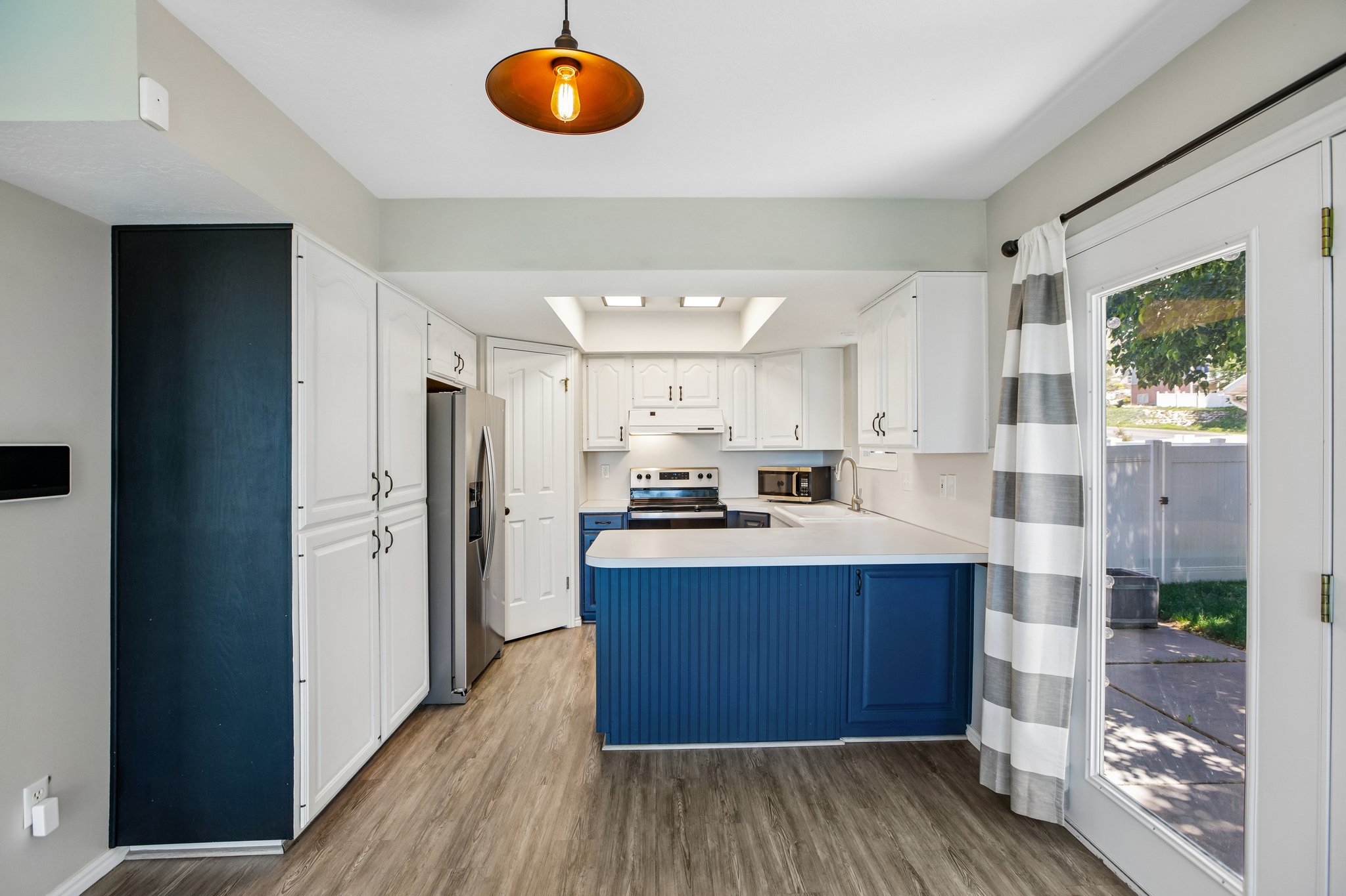 Renovated kitchen featuring a blue island, white cabinetry, stainless steel appliances, wood-finish flooring, and a glass-paned exterior door