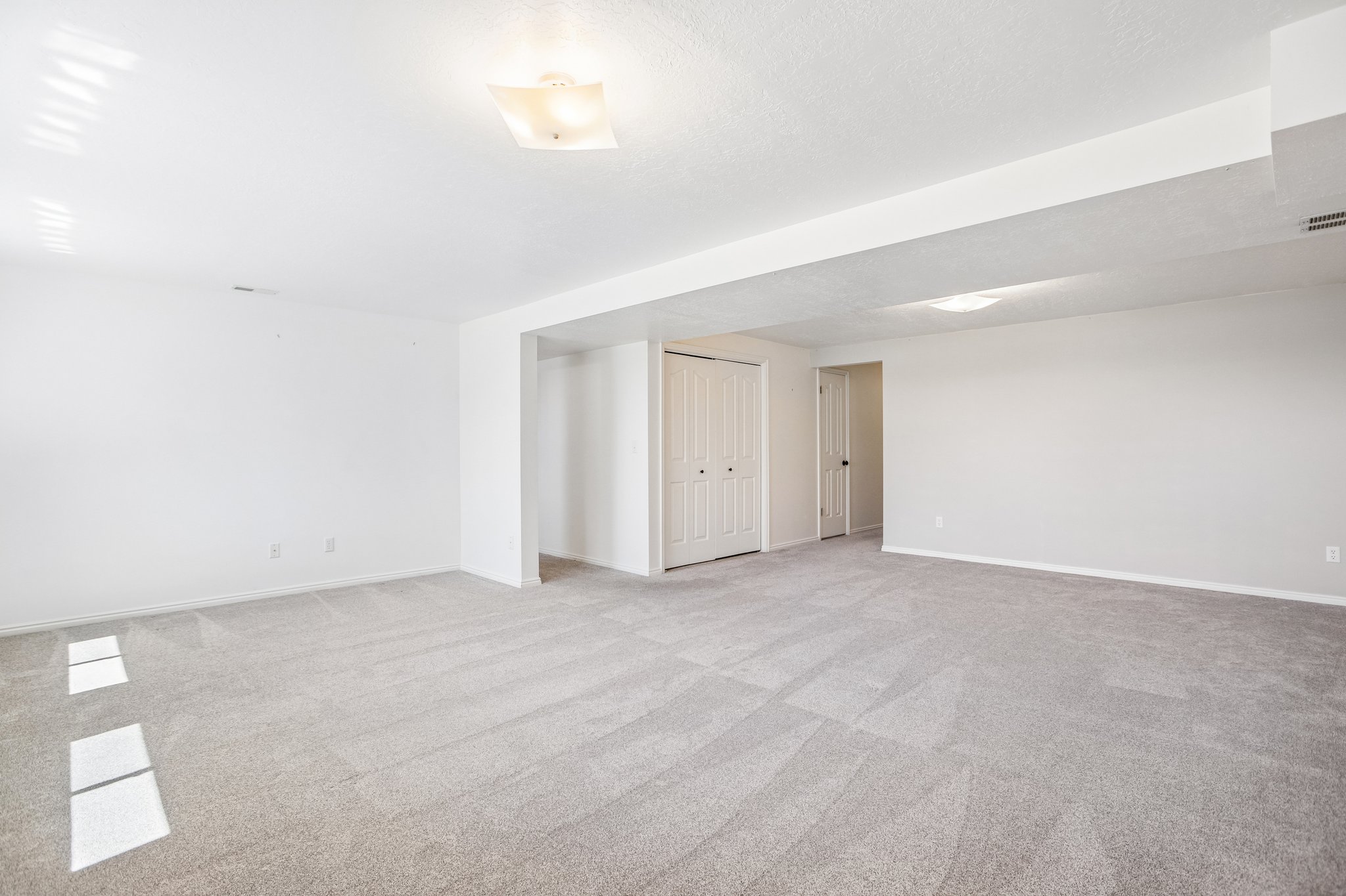 Spacious room featuring neutral carpeting, white walls, and overhead lighting