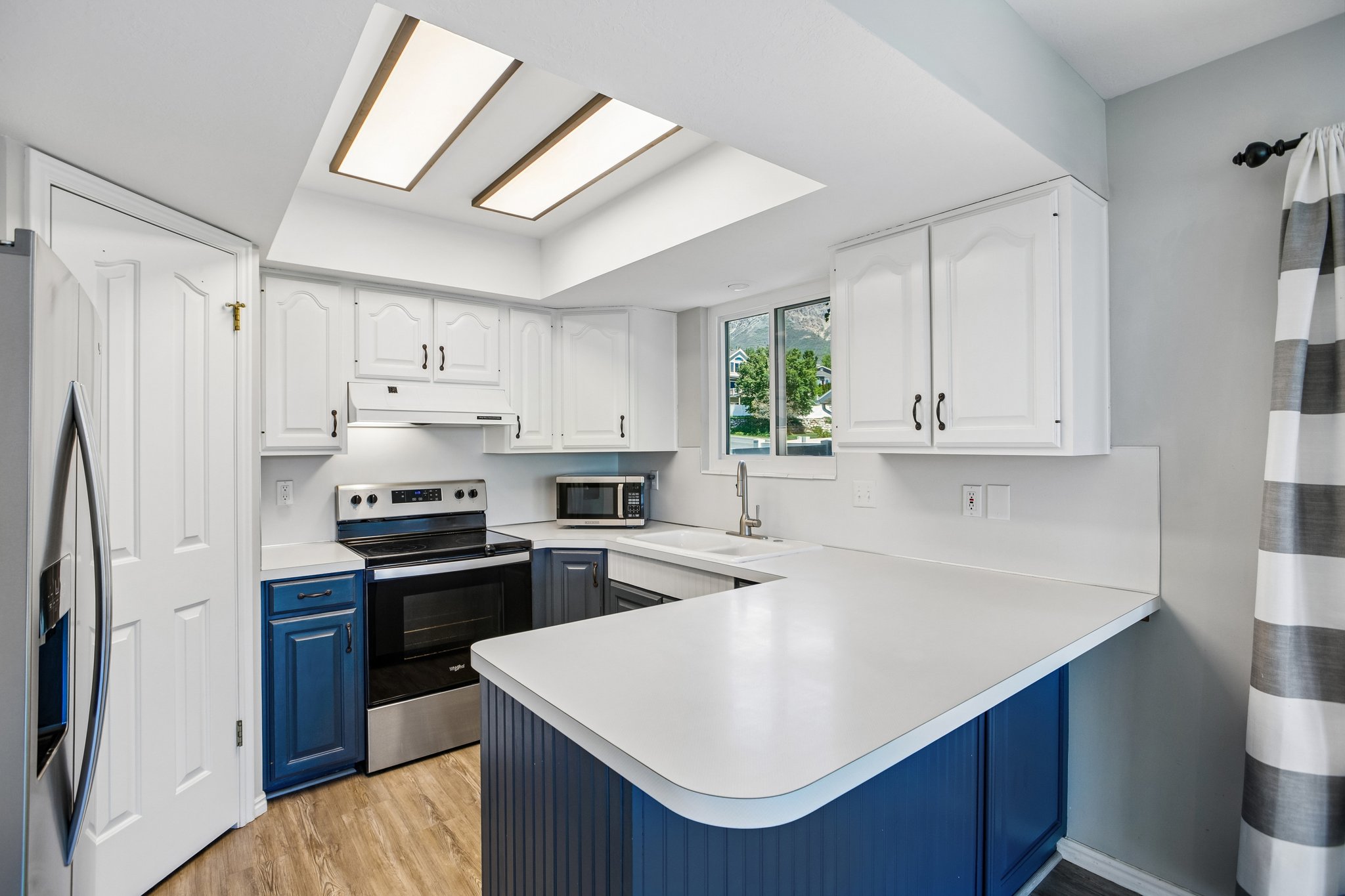 Kitchen featuring white cabinetry with black hardware, stainless steel appliances, a U-shaped countertop, and wood-finish flooring