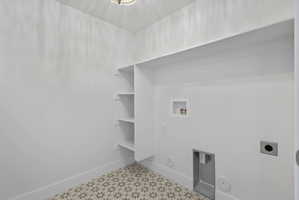Laundry space featuring patterned floor tiles, built-in shelving, an overhead light fixture, and white baseboards