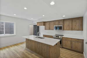 Bright kitchen featuring a central island with an undermount sink, light countertops, wood-finish flooring, and recessed lighting
