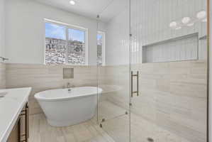 Spacious bathroom featuring a freestanding soaking tub with floor-mounted faucet, a glass-enclosed shower with subway tile surround, recessed lighting, and a white countertop vanity with dark-finish cabinetry