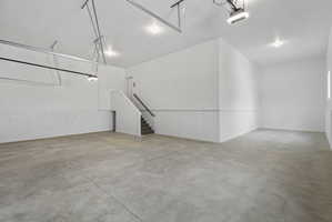 Spacious garage featuring a concrete floor, bright white walls, recessed lighting, and a built-in staircase with a handrail