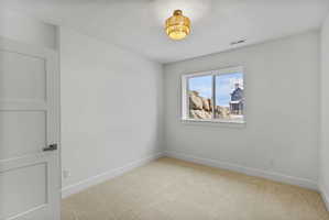 Neutral interior room featuring a light-colored carpet, white walls, and a contemporary light fixture